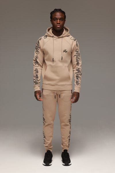 חליפת טרנינג לגבר בצבע בז’ מבית ROBERTO VINO, סוויטשירט קפוצ’ון עם כיס קדמי והדפסי לוגו שחורים על השרוולים, בשילוב מכנס תואם בגזרה צרה עם שרוך קשירה וסיומות גומי בקרסוליים.