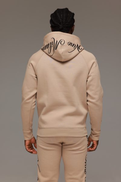 חליפת טרנינג לגבר בצבע בז’ מבית ROBERTO VINO, סוויטשירט קפוצ’ון עם כיס קדמי והדפסי לוגו שחורים על השרוולים, בשילוב מכנס תואם בגזרה צרה עם שרוך קשירה וסיומות גומי בקרסוליים.