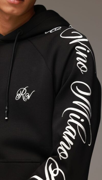 חליפת טרנינג לגבר בצבע שחור מבית ROBERTO VINO, סוויטשירט קפוצ’ון עם כיס קדמי והדפסי לוגו לבנים על השרוולים, בשילוב מכנס תואם בגזרה צרה עם שרוך קשירה וסיומות גומי בקרסוליים.